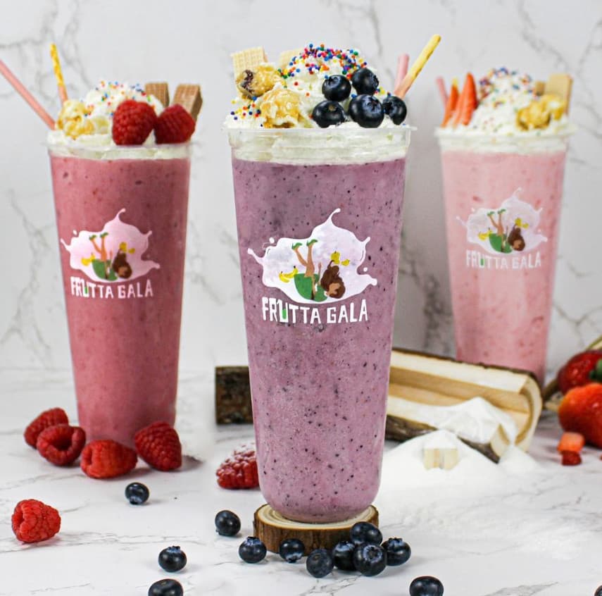 Three berry smoothies topped with whipped cream, sprinkles, wafers and fresh blueberries