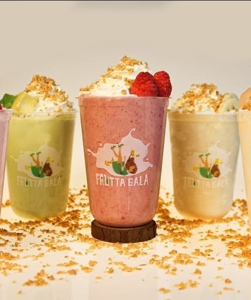 Five Frutta Gala fruit smoothies in branded cups, topped with whipped cream and crumble